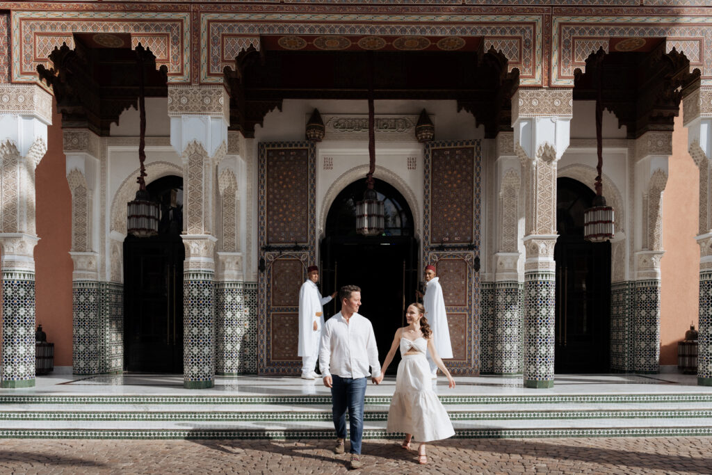 a man and woman walking in front of a la mamounia marrakech