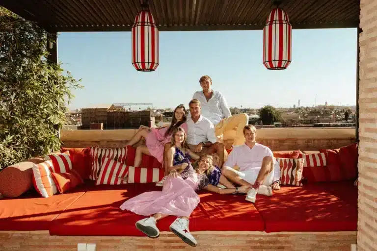 Six family members gathered on the red terrace sofa beneath striped lanterns at El Fenn, Marrakech.